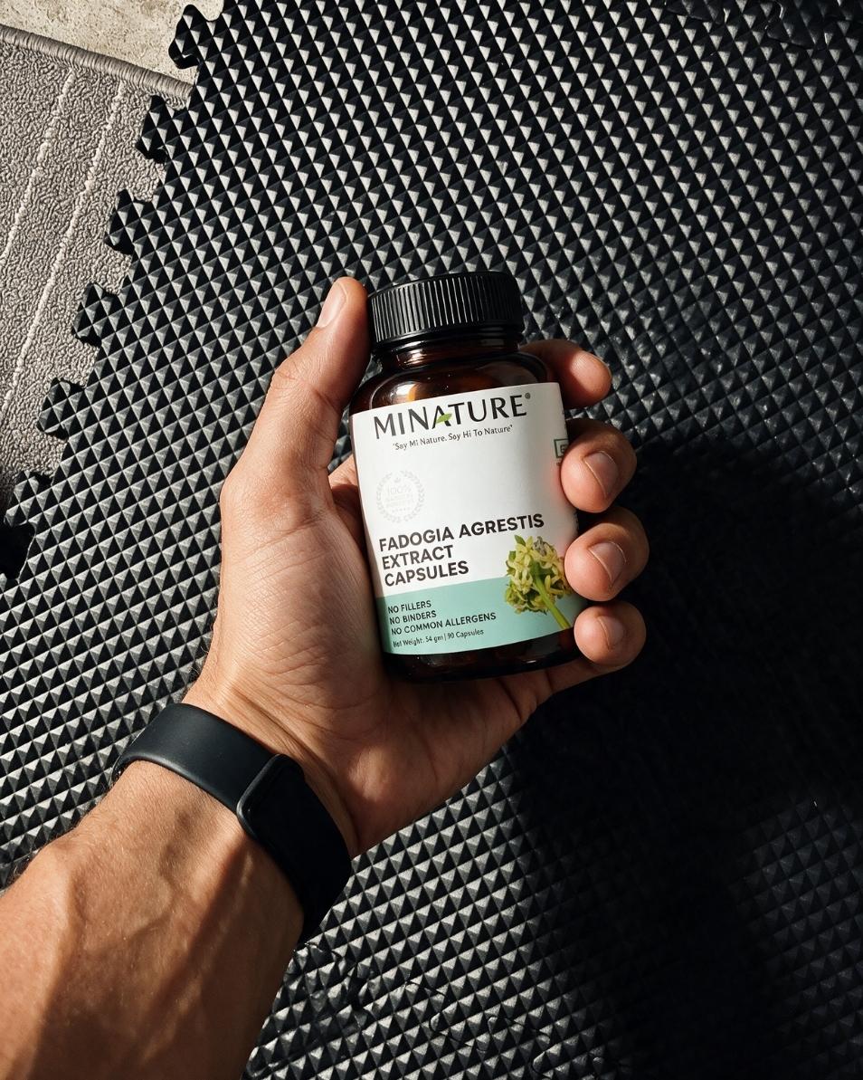 A hand holding a bottle of MINATURE Padoogia Agrestis Extract Capsules against a black textured interlocking foam mat background.